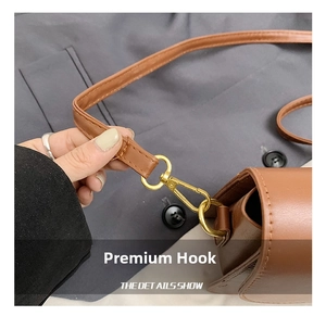 Detailed close-up of the golden metal hook and brown leather strap on a vintage underarm bag