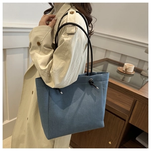 Detail of light blue canvas tote bag with black strap and knot shown on person