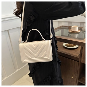 Detail of a beige crossbody bag with V-shaped quilted pattern and stylish top handle