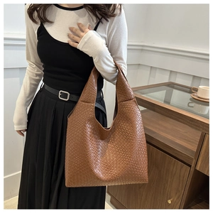 Detail of a large brown woven tote bag featuring intricate cross-weave texture and wide strap