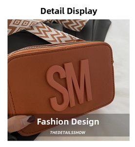 Detailed view of the brown camera bag featuring the SM embossed logo and wide woven strap