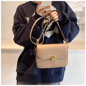 Detail of a chic beige crossbody bag with a gold metal clasp shown on a model