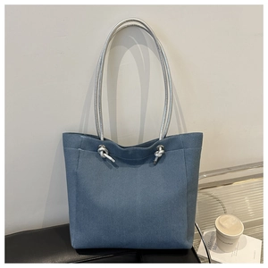 Détail du sac cabas en toile denim bleue avec anses en corde argentée sur un banc