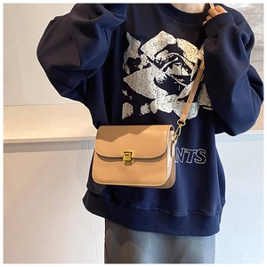 Detail of a beige leather square bag with gold buckle on a model for size perspective