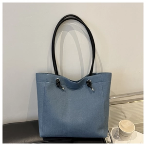 Sac fourre-tout en denim bleu avec anses à nœuds noirs posé sur un banc en cuir au café