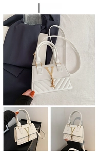 Close-up of white leather handbag featuring gold V-logo, tassel detail and quilted stitching