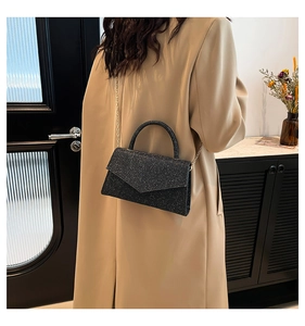Detail of black glitter crossbody bag with gold chain strap on model wearing wool coat