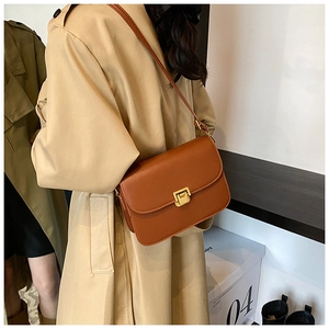 Detail of a brown leather crossbody bag with a square metal buckle on a female model