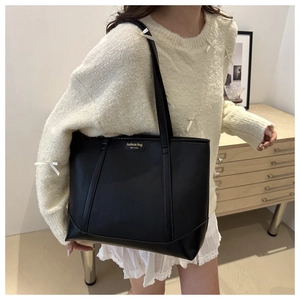 Detail of black pebbled leather tote bag with gold lettering and sturdy shoulder straps