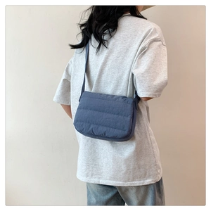 Blue quilted nylon puffer crossbody bag shown with adjustable strap on model