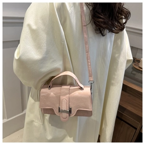 Detail of light pink crossbody bag with silver buckle worn over a beige coat