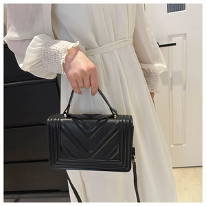 Detail of black V-quilted faux leather crossbody bag with top handle and gold hardware