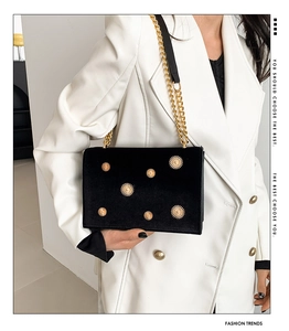 Detail of black velvet chain bag with gold sun ornaments worn over a white suit jacket
