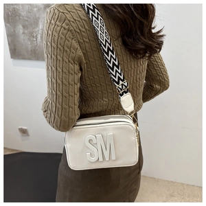 Detail view of a white textured crossbody bag with SM logo and geometric wide strap