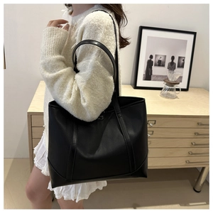 Detail of a black large-capacity tote bag in pebble leather worn on a woman's shoulder