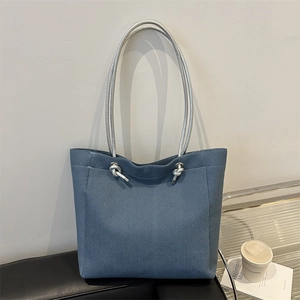 Sac cabas minimaliste en jean bleu avec anses en corde argentée sur un banc dans une pièce