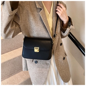 Close-up of minimalist black matte leather crossbody bag with gold square buckle lock