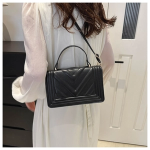 Rear view of model wearing a black quilted crossbody bag with V-shaped stitching detail