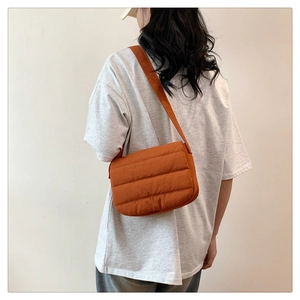 Back view of a model wearing a burnt orange quilted shoulder bag with a wide strap