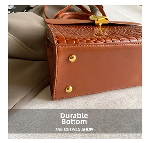 Detailed view of the brown leather bag bottom featuring gold studs and alligator texture