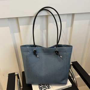 Sac cabas bleu en toile denim avec anses en cuir noir et nœud décoratif sur chaise