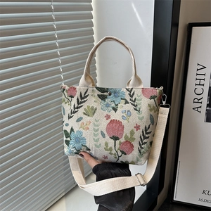 Floral embroidered canvas tote bag with adjustable strap and top handle shown in soft light