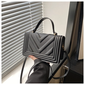 Detail of the black quilted crossbody bag with chevron pattern and gold metal hardware