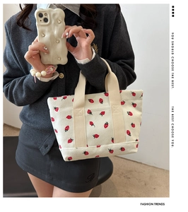 Detail of off-white corduroy tote bag featuring red strawberry prints and wide strap