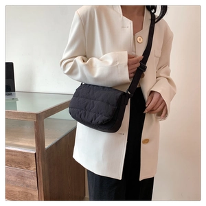 Detail of a black quilted crossbody bag with adjustable wide fabric strap on a table