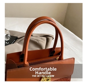 Close-up of brown faux leather handbag showing dual handles and gold zipper hardware