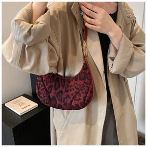 Close-up of leopard print crescent bag in dark red suede under arm with gold hardware