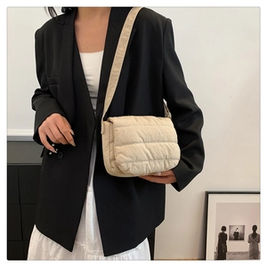Close-up of beige quilted crossbody bag with horizontal stitching worn by model