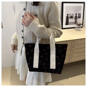 Close-up of black corduroy tote bag featuring red strawberry embroidery and canvas handles