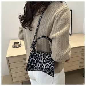 Detailed view of leopard print crossbody bag with curved base and adjustable shoulder strap