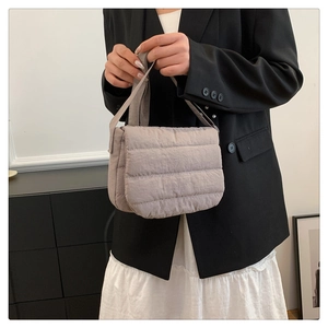 Close-up of a light grey quilted crossbody bag showing soft puffy fabric and wide strap