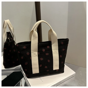 Détail d'un sac cabas en velours côtelé noir avec broderies fraises et anses en toile
