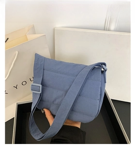 Close-up of blue quilted fabric crossbody bag showing soft puffer texture and strap