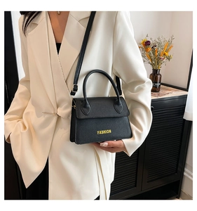 Detail of black crossbody bag with yellow FASHION text on model in white suit