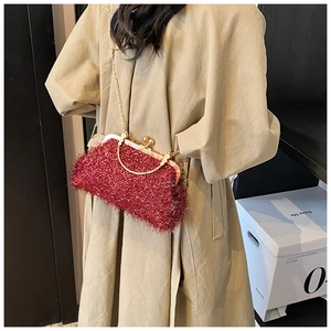 Red plush evening shell bag with gold chain worn over a khaki trench coat