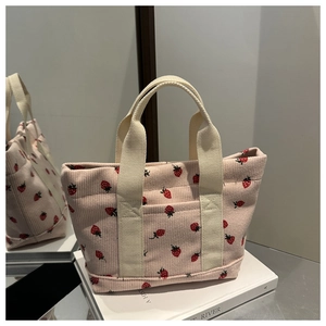Détail du cabas en velours côtelé rose avec fraises et poignées beiges sur livre