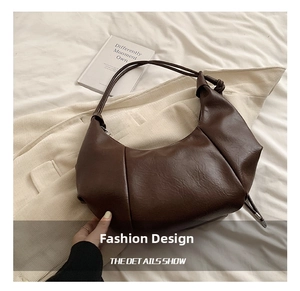 Detail of a brown crescent hobo bag with a knotted shoulder strap and pebbled leather texture