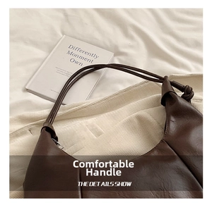 Close-up of brown textured leather shoulder bag with sleek handle and knot detail