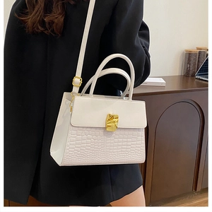 Detail of white crocodile embossed handbag with gold geometric clasp on female model