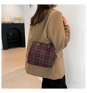 Detailed shot of retro plaid wool bucket bag with metal chain strap on model's shoulder