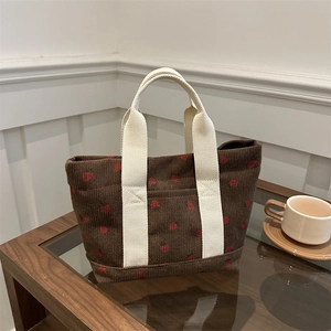 Sac tote en velours marron à motif fraise et anses blanc cassé sur table en bois
