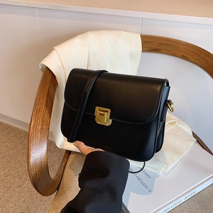 Classic black leather crossbody bag with golden square lock on a light wooden seat