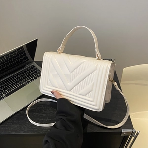 Creamy white V-quilted small square crossbody bag with top handle in office setting