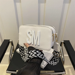 White camera crossbody bag with SM logo and black-white patterned wide shoulder strap