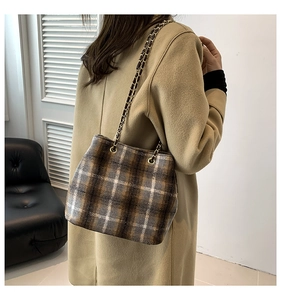 Detail of wool plaid bucket bag with gold chain strap on model's shoulder in brown