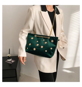 Close-up of dark green velvet shoulder bag with sunburst gold studs and chain strap